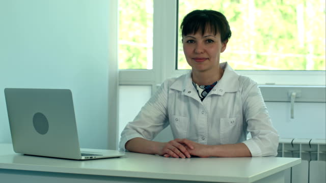 Female-doctor-working-at-office-desk-with-laptop-and-smiling-at-camera