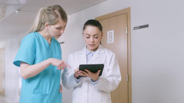 Im-Krankenhaus-sprechen-beschäftigt-Ärzte,-mit-Tablet-Computer-stehen-auf-dem-Flur.-Neue-moderne-voll-funktionsfähige-medizinische-Einrichtung.