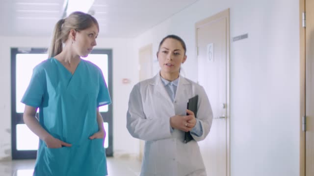Nurse-and-Doctor-Walk-Through-Hospital-Hallway,-Talking,-Discussing-Modern-Medical-Procedures.-Professional-People-Saving-Lives.