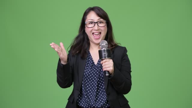 Mature-beautiful-Asian-businesswoman-as-newscaster-using-microphone