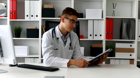 Young-doctor-showing-paper-and-smiling-at-camera