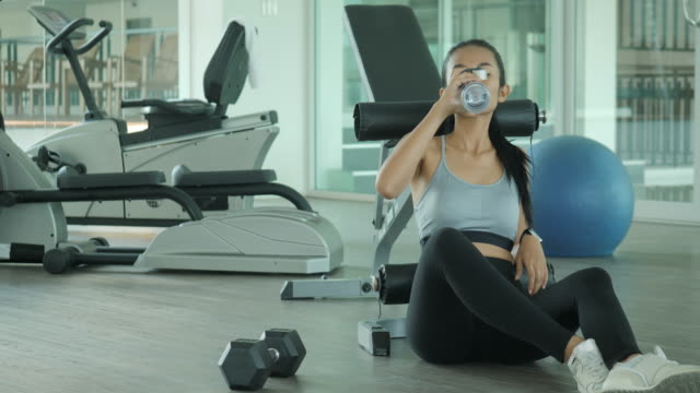 Asian-woman-in-gym-drink-water-after-exercise