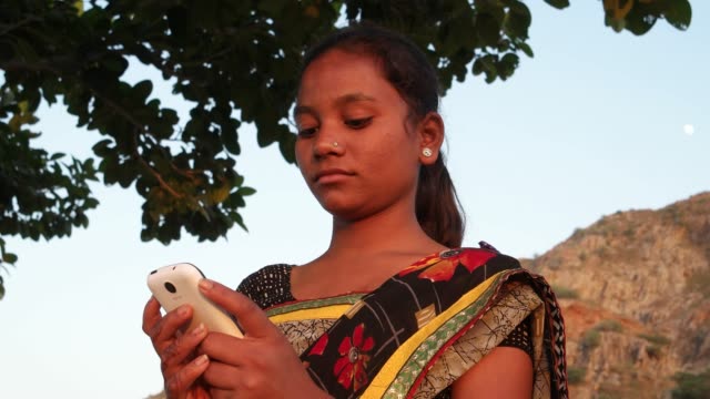 Teenager-Mädchen-Zifferblätter-Gespräche-Idee-Mobile-Smartphone-umzusehen-Natur-Hill-Top-Lächeln-freude-freudig-Spaß-Panorama-Sicht-Sonnenuntergang-Dämmerung-an-einem-heißen-Sommertag-in-Indien-handheld-stabilisierten-Sand-anzeigen