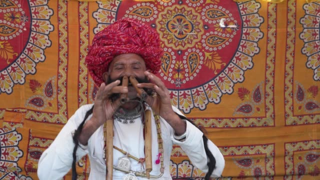 Hand-Held-Rajasthani-ältere-Männchen-beginnt-das-Flötespielen-mit-seiner-Nase-vor-einem-bunten-Stoff-Zelt