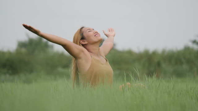 Joyful-Woman-Sitting-on-the-green-field-and-raising-her-hand-refresh-life