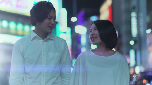 Japanische-junge-und-Mädchen-paar-gehen-und-sprechen.-Im-Hintergrund-unscharf-Werbetafeln-und-Citylights-in-der-Nacht.