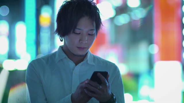 Porträt-des-schönen-Alternative-japanischen-jungen-mit-Smartphone.-Im-Hintergrund-Plakate-Großstadt-Werbung-Lichter-leuchten-in-der-Nacht.