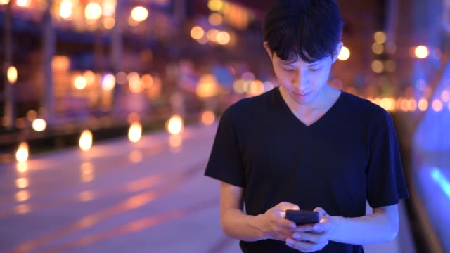 Porträt-des-asiatischen-Menschen-draußen-in-der-Nacht-mit-Handy