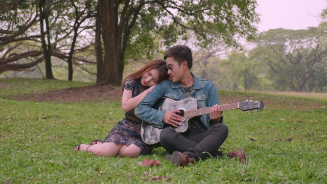 Joven-pareja-asiática-pasar-tiempo-juntos-en-el-parque,-tocar-la-guitarra,-hablando,-disfrutando.