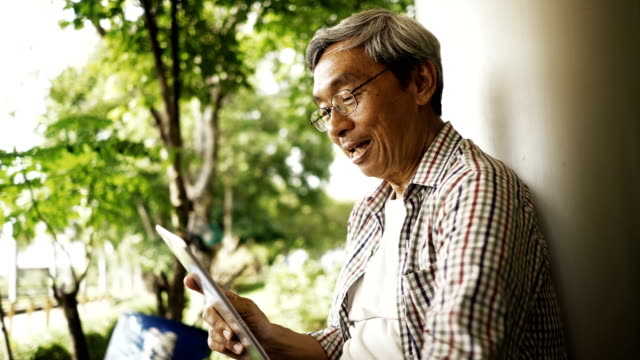 Asiatischer-senior-Mann-mit-Tablet,-allein-auf-der-Bank-im-Park-sitzen