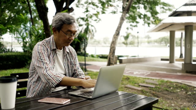 Asian-senior-man-shopping-online-with-his-notebook-in-the-park