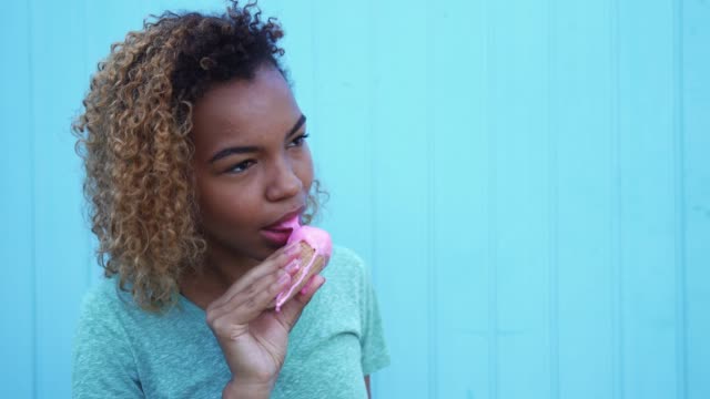 young-black-girl-eating-pink-ice-cream-and-smiling-at-blue-wall-background