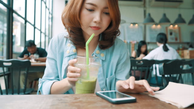 Fröhlich,-glücklich-junge-Asiatin-sitzen-trinken-Eistee-grüner-Tee-im-Café-mit-Smartphone-zum-sprechen,-lesen-und-SMS.-Frauen-Lifestyle-Konzept.