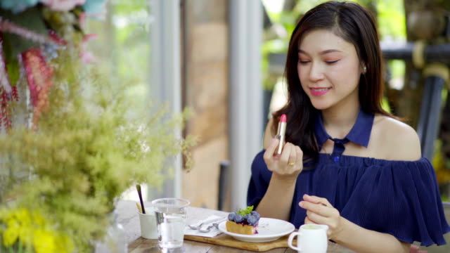 woman-doing-make-up-with-lipstick-in-a-café
