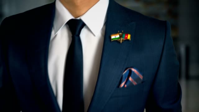 Empresario-caminando-hacia-cámara-con-amigo-país-banderas-Pin-India---Camerún
