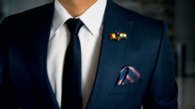Businessman-Walking-Towards-Camera-With-Friend-Country-Flags-Pin-Romania---India