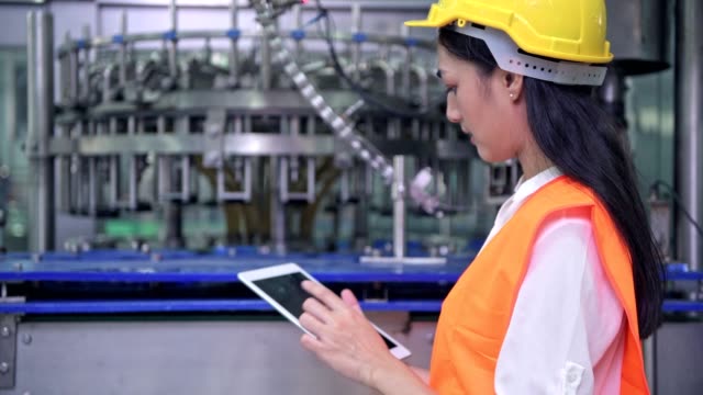 Woman-industrial-engineer-at-work-in-factory.-Beautiful-young-chinese-engineer-working-in-large-factory.-With-safety-helmet-and-jacket.-High-tech-automatic-machine-in-background.