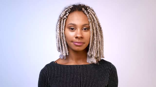 Young-African-girl-with-dreadlocks-smiling-and-looking-at-camera,-White-wall-in-the-background.