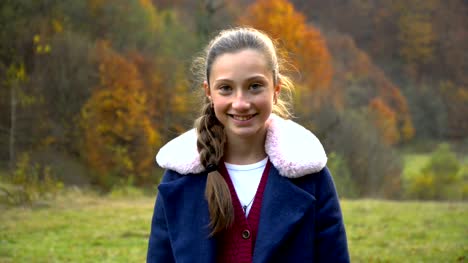 A-beautiful-young-girl-is-standing-in-the-autumn-forest,-looking-at-the-camera-and-smiling.-She's-happy.