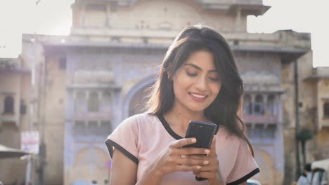 A-Young-and-attractive-woman-on-a-city-street-and-using-smartphone-or-cellphone-with-a-smile.