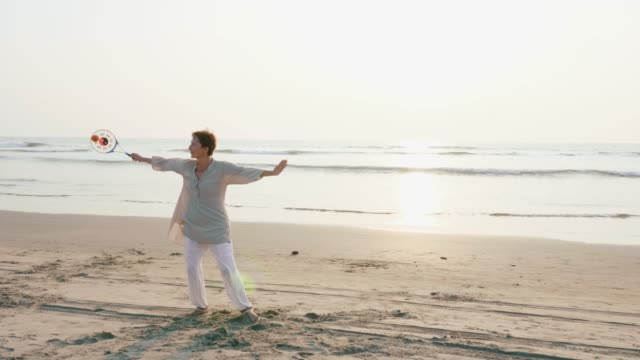 Senior-woman-practicing-tai-chi-balloon-ball-on-the-beach-at-sunset