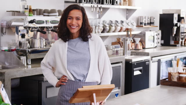 Mixed-race-female-coffee-shop-owner-smiling-behind-counter