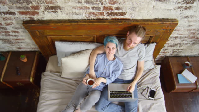 Happy-Hipster-Couple-Sitting-on-Bed