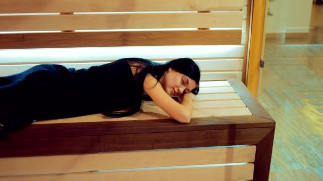 Beautiful-girl-lies-on-a-wooden-bench-in-the-sauna-behind-a-glass-door.-Girl-lies-with-her-eyes-closed.-Span-camera.-Portrait-view