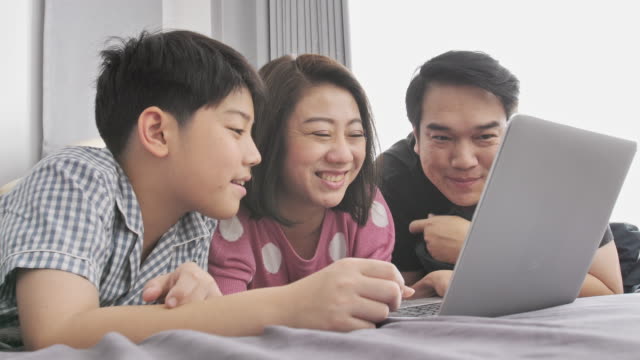 Feliz-familia-padre-madre-e-hijo-viendo-la-computadora-portátil-y-te-diviertes,-lenta-4K-Asia-resto-familiar-en-cama-con-el-ordenador-portátil