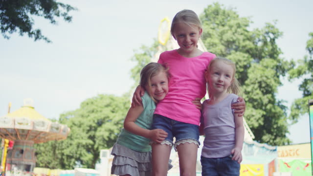 Three-little-girls-at-a-fair-give-a-group-hug-and-smile-at-the-camera