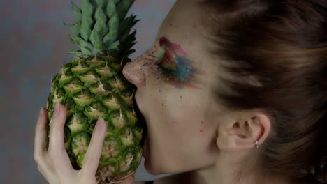 4-k-Aufnahme-einer-Frau-mit-bunten-Make-up-beißen-Ananas