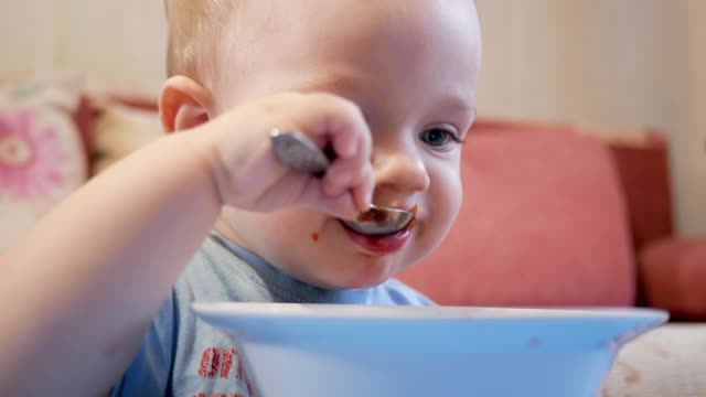 Un-atractivo-chico-de-2-años-de-edad-es-comer-sopa-roja-sí-mismo.-Cuchara-y-las-manos-fluyendo-líquido.-El-concepto-de-alimentación-saludable-de-los-niños