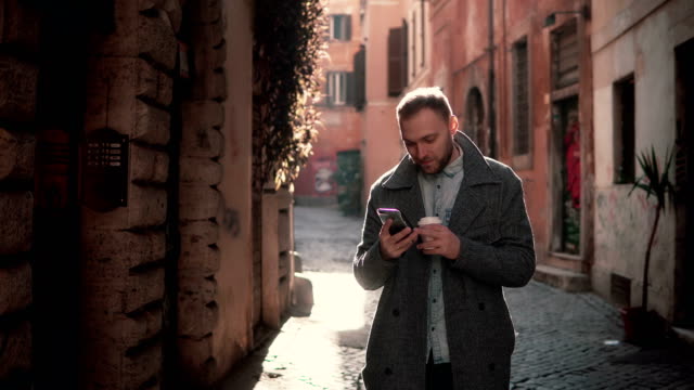 Porträt-des-jungen-glücklicher-Mann-zu-Fuß-in-die-Stadt-und-mit-Smartphone.-Männchen-das-Internet-surfen-und-Holding-Tasse-Kaffee