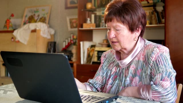 Eine-ältere-Frau-prüft-die-Nachrichten-in-sozialen-Netzwerken-auf-einem-Laptop-zu-Hause.-Sie-sitzt-am-Tisch