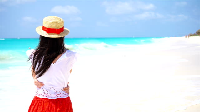 Back-view-of-beautiful-woman-in-hat-on-summer-holidays-on-white-beach.