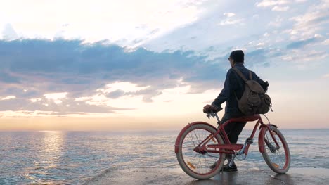 Junge-Frau-sitzt-auf-Vintage-Fahrrad-am-Meer-im-schönen-Sonnenaufgang