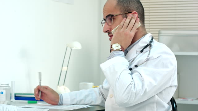 Médico-joven-árabe-tener-conversación-de-teléfono-en-su-oficina