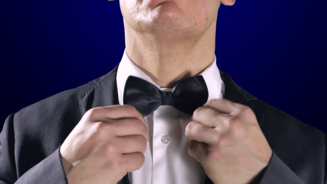 Man-Fixing-Bow-Tie,-Close-Up-Tuxedo-Suit,-Dark-Blue-Background