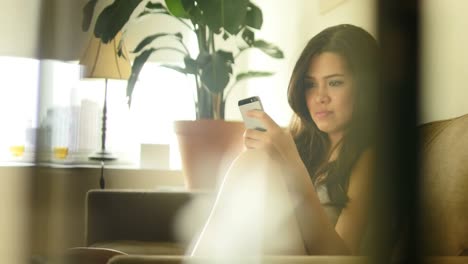 Attractive-Asian-Woman-Sitting-on-Couch-at-Her-Home.-Using-A-Smartphone-and-Sending-Text-Messages.