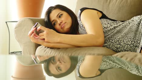 Attraktive-asiatische-Frau-liegt-auf-dem-Sofa-in-ihrem-Haus.-Mit-einem-Smartphone-und-senden-von-Textnachrichten.