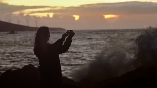 Ein-Mädchen-macht-ein-Meer-Sonnenuntergang-Foto-mit-einem-mobilen-Gerät