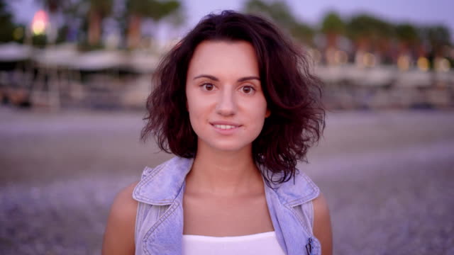 Porträt-einer-jungen-Frau-mit-kurzen-und-lockigen-Haaren,-trägt-eine-Jeans-und-steht-im-Sommer-am-Strand