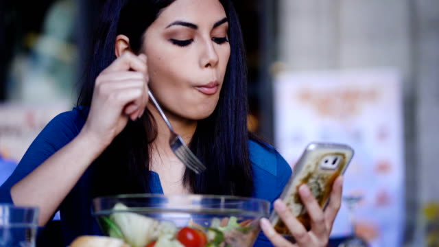 Asiatische-Frau-SMS-auf-Smartphone-und-Salat-im-Restaurant-Essen