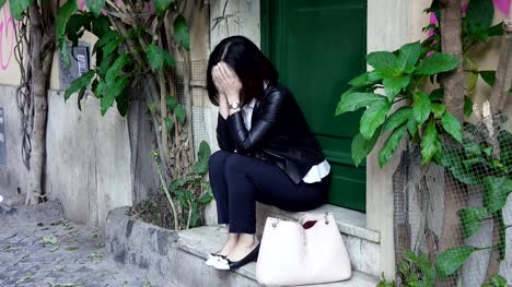 Sad-asian-woman-walking-down-the-street-and-sits-down-a-step-and-despairs