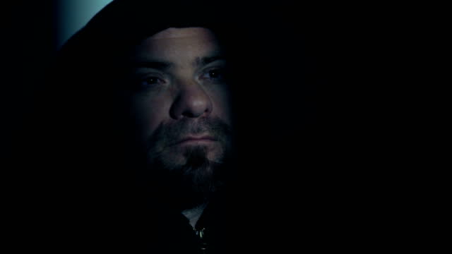 Man-with-thoughtful-hood-in-the-dark-opens-his-eyes-and-looks-at-the-light