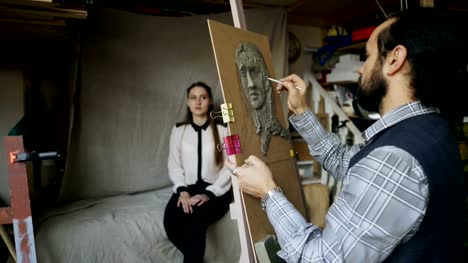 Skilled-sculptor-works-with-plasticine-on-canvas-to-create-woman's-face-of-posing-model-in-art-studio