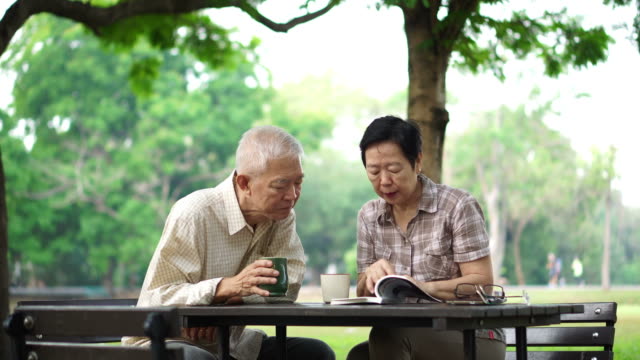 Asian-senior-retire-couple-drink-coffee-and-read-book-in-park