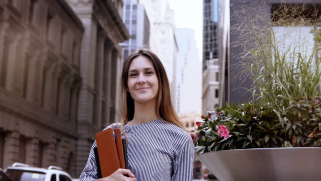 Portrait-of-young-beautiful-successful-businesswoman-near-office-building-in-New-York,-America.-Female-holds-documents