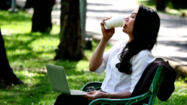 Mujer-de-negocios-asiáticos-usando-laptop-y-tomando-café-en-el-parque.