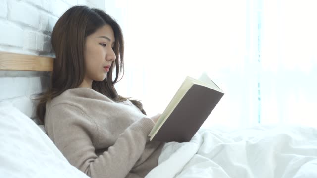 Lebensstil-glücklich-junge-asiatische-Frau-liegend-auf-dem-Bett-Buch-Lesevergnügen-in-casual-Kleidung-zu-Hause-zu-genießen.-Entspannte-Lifestyle-Frau-Konzept.